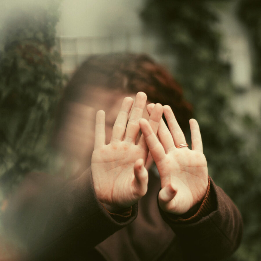 two clear hands held out in front of a face that is blurry to communicate boundaries and saying no